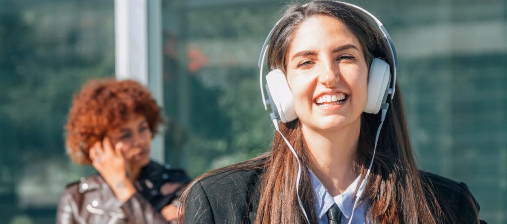 Mujer joven escucha un pódcast con auriculares mientras a su espalda otra persona conversa, imagen del punto ciego del social listening