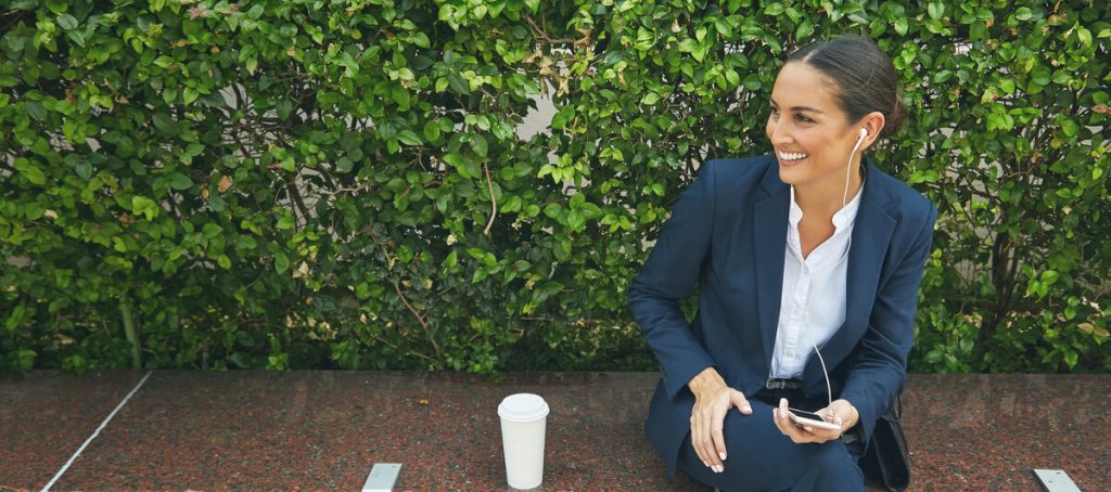 Profesional con auriculares escucha un pódcast al aire libre mientras consulta el móvil, audiencia del podcasting en España y Latinoamérica