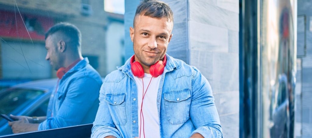 Hombre con auriculares rojos y móvil en la calle mientras otro hombre consulta su teléfono al fondo