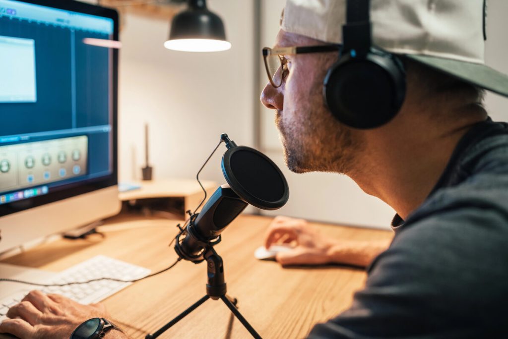 Podcaster con auriculares edita el audio de una entrevista en el ordenador