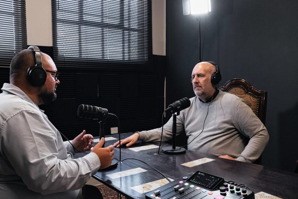 Presentador e invitado con auriculares conversan frente a los micrófonos en un estudio de pódcast